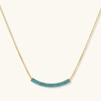Gold-plated curved necklace and hoop earrings with turquoise cubic zirconia stones on white background.