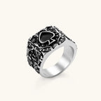 Silver-tone 316L stainless steel signet ring with black enamel spade motif and intricate floral scrollwork relief detail.