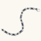 Close-up of the stainless steel link bracelet with blue CZ stones and baroque scroll engravings.