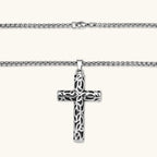 Silver stainless steel Celtic cross pendant with filigree vine pattern on a box chain, against a cream background.