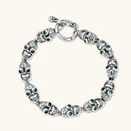Silver stainless steel skull link bracelet with green crystal eye sockets and engraved detailing, toggle clasp closure.