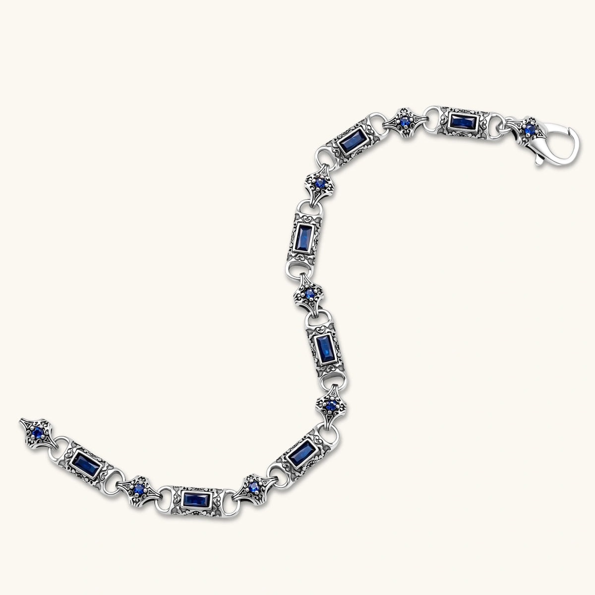 Close-up of the stainless steel link bracelet with blue CZ stones and baroque scroll engravings.