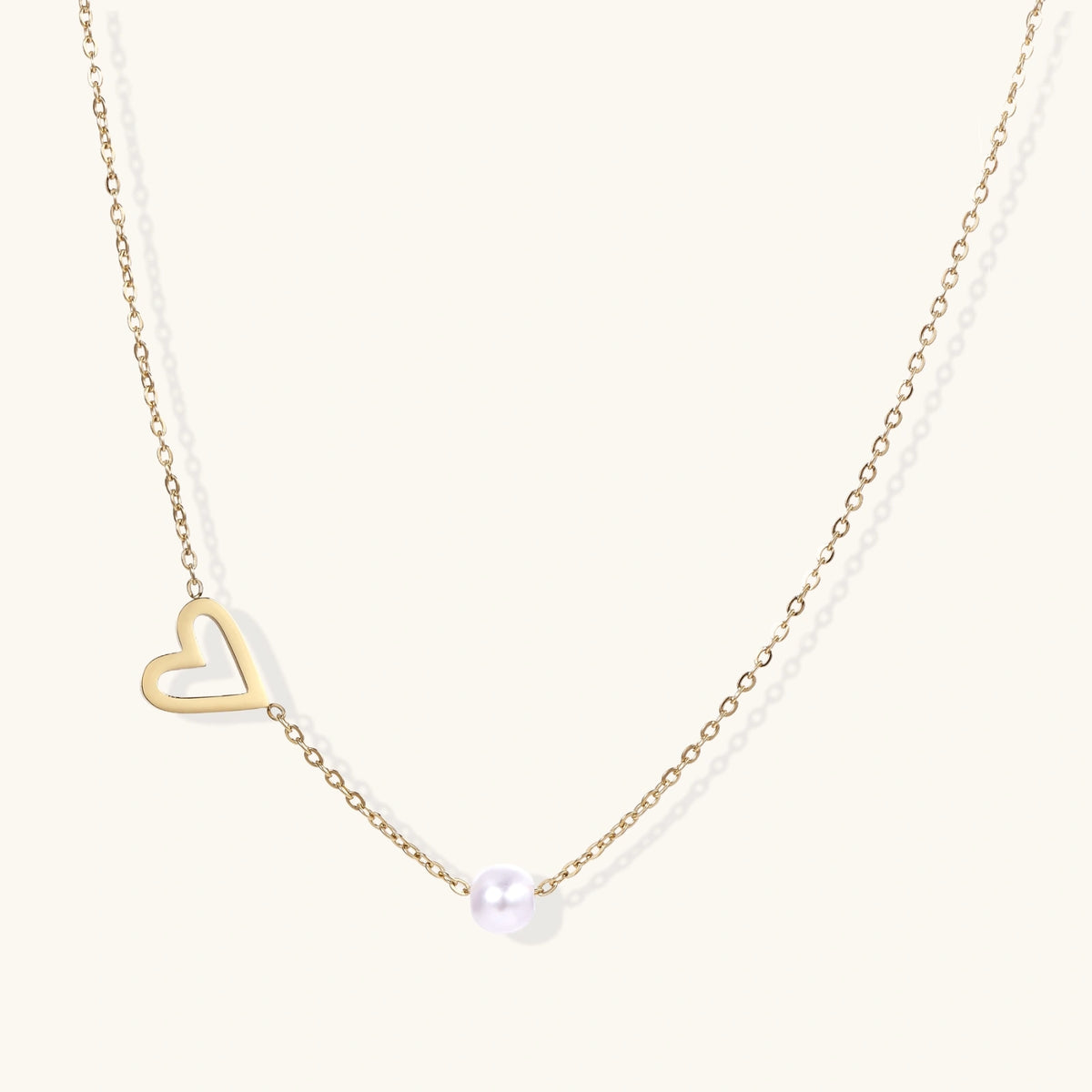 Front view of the gold asymmetric open heart charm with a single pearl bead on a fine chain.
