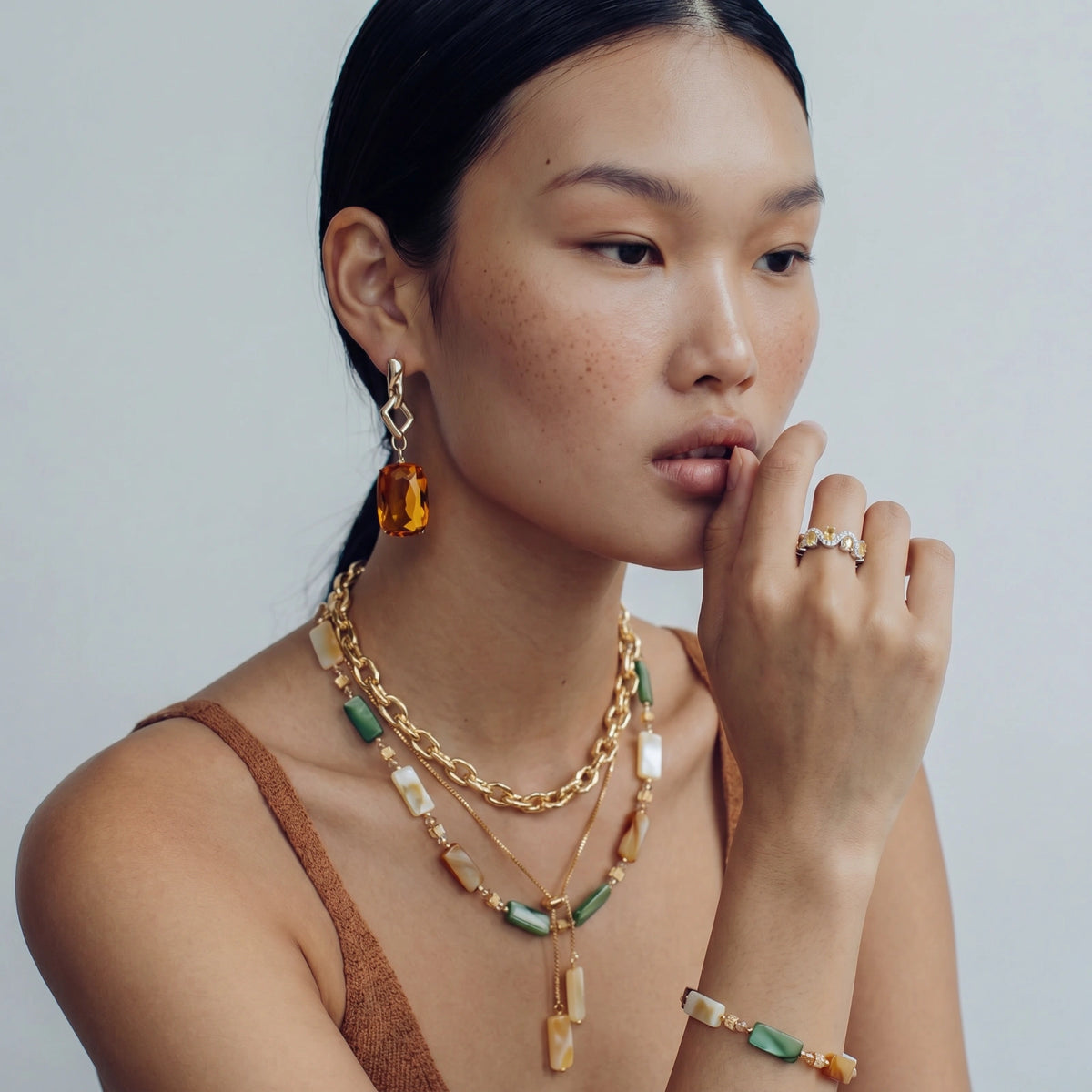 Detail view of the gold-plated bracelet with geometric shell beads in green, orange, and white.