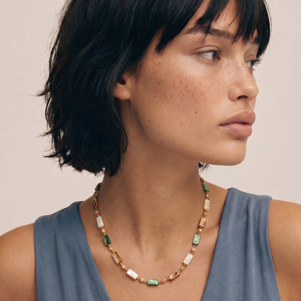 Detail view of the 18K gold-plated necklace with natural shell beads in green, amber, and cream tones.